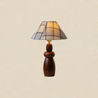 A tall Clérachic table lamp with a plaid shade and a stacked, tapering wood base, on a plain beige backdrop.
