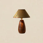 A Clérachic table lamp with a straw weave shade and a tall wood base carved with horizontal ribs, on a beige backdrop.