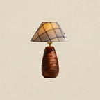 Tall wood base carved with horizontal ribs under a plaid shade, this Clérachic table lamp on a plain beige backdrop.