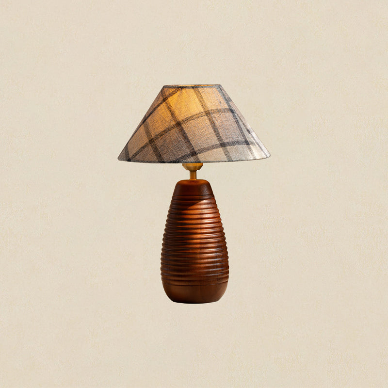 Tall wood base carved with horizontal ribs under a plaid shade, this Clérachic table lamp on a plain beige backdrop.