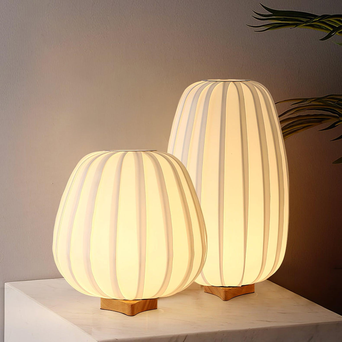 Warm light fills both ribbed white shades of this Clérachic table lamp pair, set on a marble surface against a dim wall.