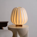 Front view of the round Clérachic table lamp lit warm on a stone side table, its wooden base visible beneath the ribbed shade.