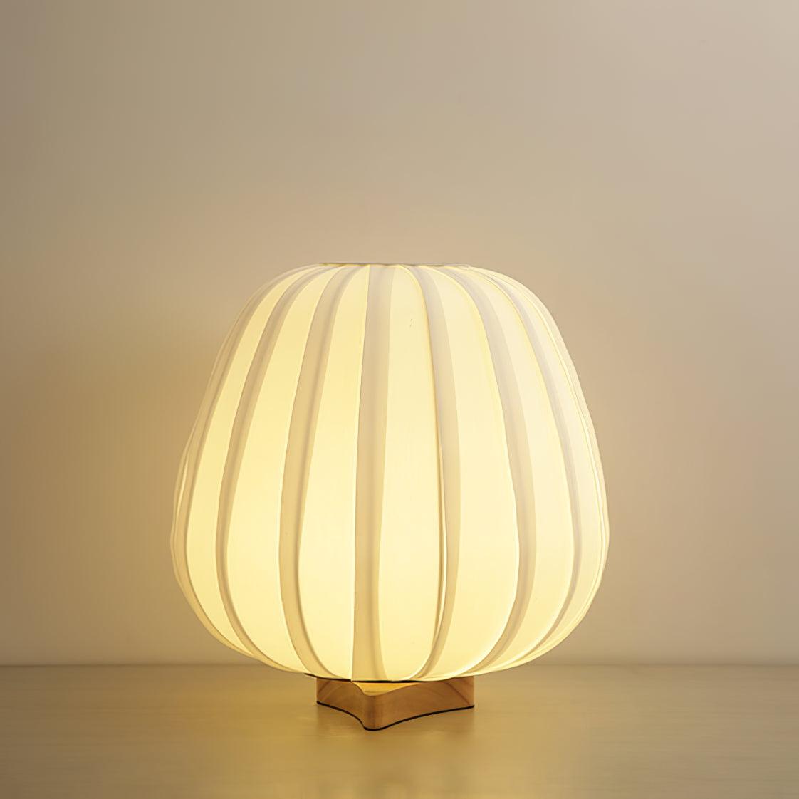 Glowing warm and bright, the round Clérachic table lamp sits on a pale wooden surface against a beige wall.