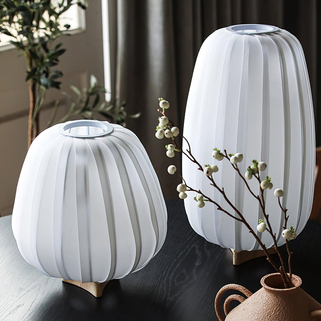 Beside a vase of white berry stems, two unlit Clérachic table lamps show their white ribbed shades on a dark wooden table.