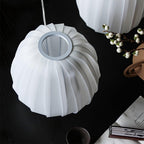 Top-down view of an unlit Clérachic shade, its ribbed white fabric gathering at a round opening, on a black table with white berries.