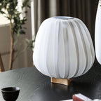 Close view of a white ribbed Clérachic shade, unlit, on a wooden base on a dark table with a small black cup.