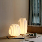 A round and a tall Clérachic lamp glow on a tatami-style mat beside a tea set, with teal curtains at the window.