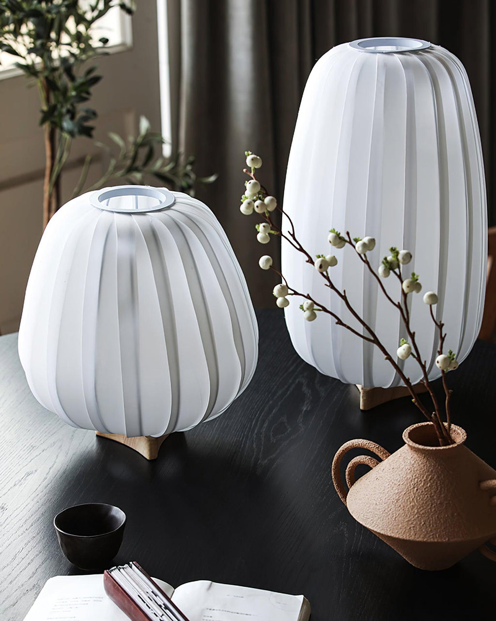 Two unlit Clérachic table lamps with white ribbed shades stand on a dark table beside a clay vase of berries.