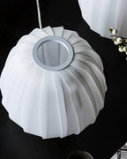 Underside view of a white ribbed Clérachic shade and its round metal-edged opening, on a black table with white berries.
