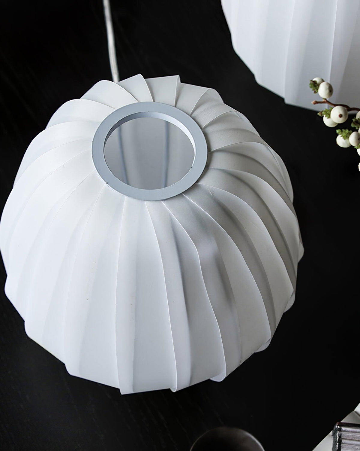 Underside view of a white ribbed Clérachic shade and its round metal-edged opening, on a black table with white berries.