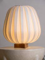 A lit Clérachic table lamp rests on a stone side table, its ribbed fabric shade glowing warm against a grey wall.