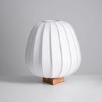 Unlit Clérachic table lamp in white ribbed fabric on a wooden base, shown at an angle against a grey backdrop.
