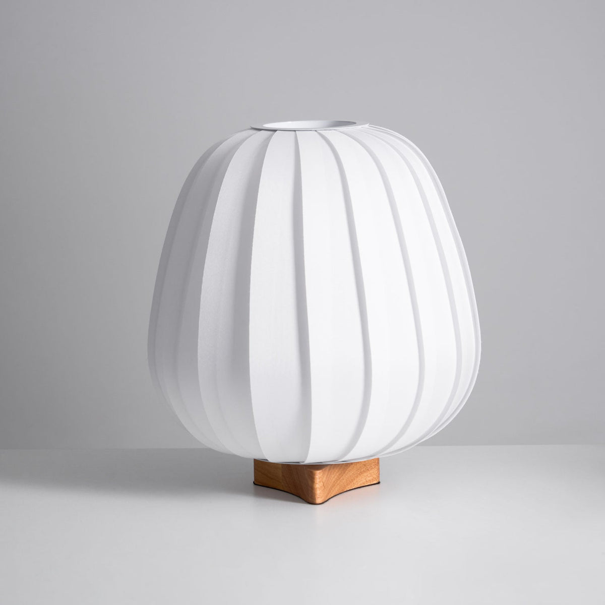 Unlit Clérachic table lamp in white ribbed fabric on a wooden base, shown at an angle against a grey backdrop.
