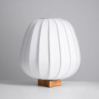 A white ribbed Clérachic table lamp on a wood base, unlit, seen straight on against a grey backdrop and pale surface.