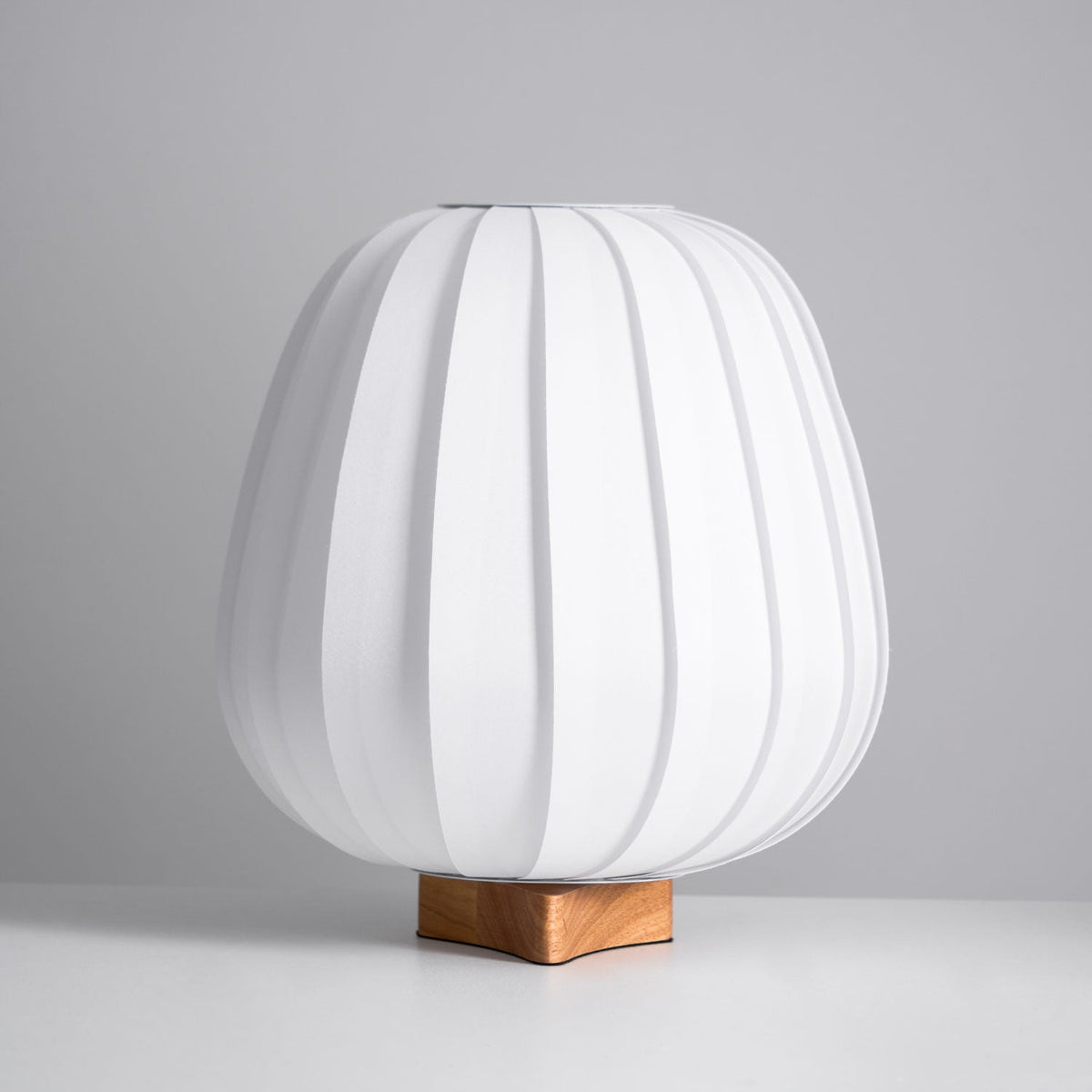 A white ribbed Clérachic table lamp on a wood base, unlit, seen straight on against a grey backdrop and pale surface.