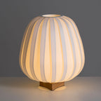 Warm light glows through the ribbed fabric of this Clérachic table lamp, with its top opening and wooden base on a grey surface.