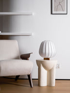 A small Clérachic table lamp stands on a stone side table beside a boucle chair, a shelf and a framed line drawing behind.
