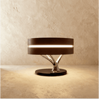 Clérachic drum table lamp with a dark wood shade, glowing band and chrome branch stem on a black base, on limewash.