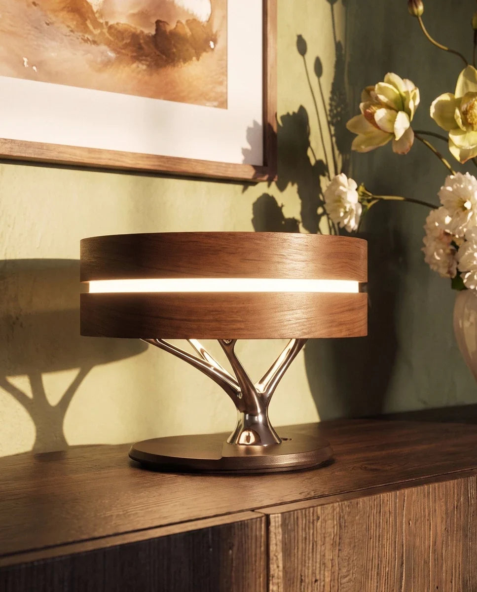 Clérachic table lamp close up on a wooden sideboard, its warm light band between two wood rings above a chrome branch stem.