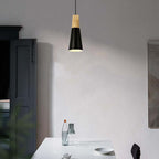 A slim black Clérachic cone pendant, its wood cap catching light, hangs unlit above a white dining table.