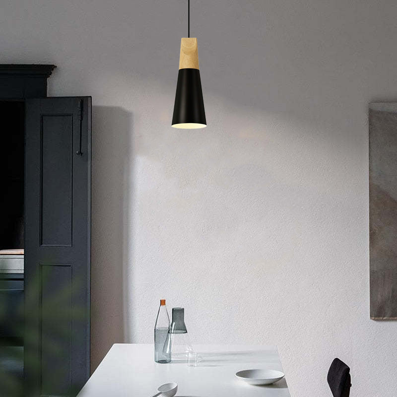 A slim black Clérachic cone pendant, its wood cap catching light, hangs unlit above a white dining table.