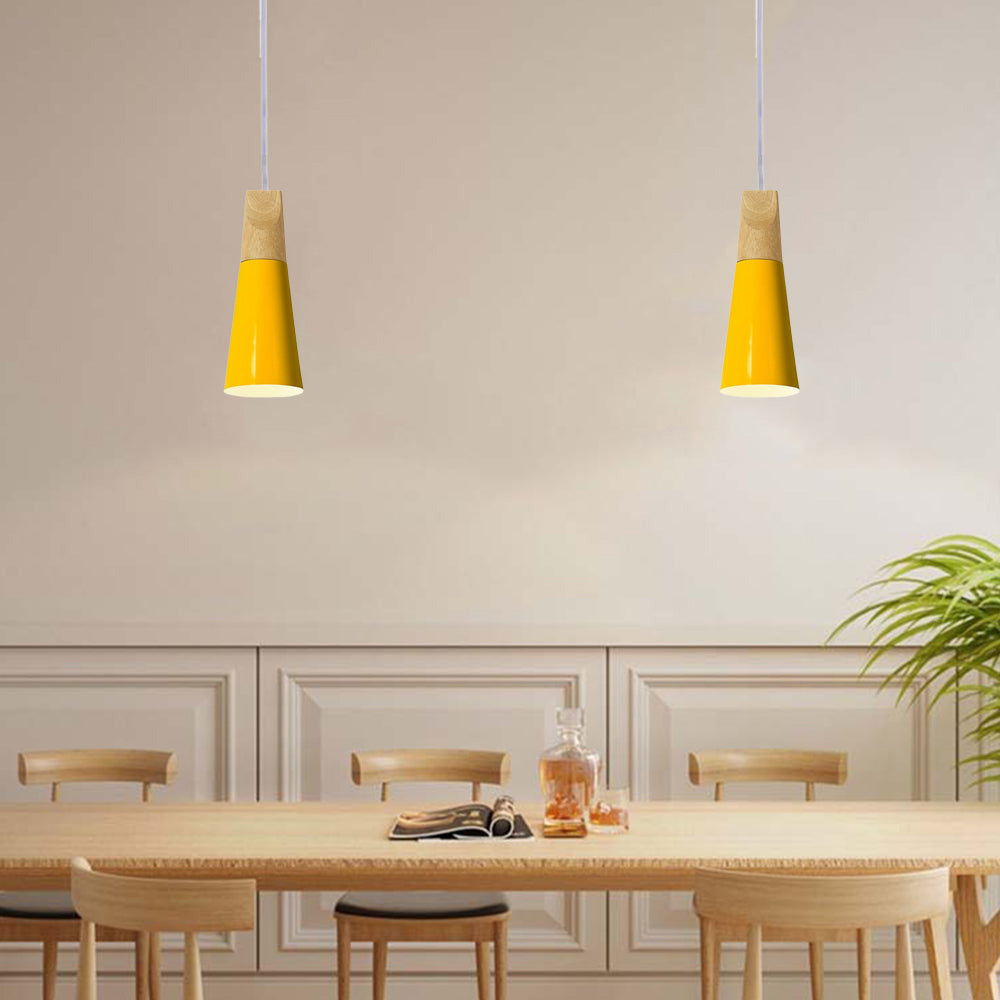 Two slim yellow Clérachic cone pendants hang in a row above a long wooden dining table set for a meal.