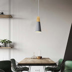 A slim grey Clérachic cone pendant is lit above a wooden table flanked by wire-frame chairs in a loft-style room.