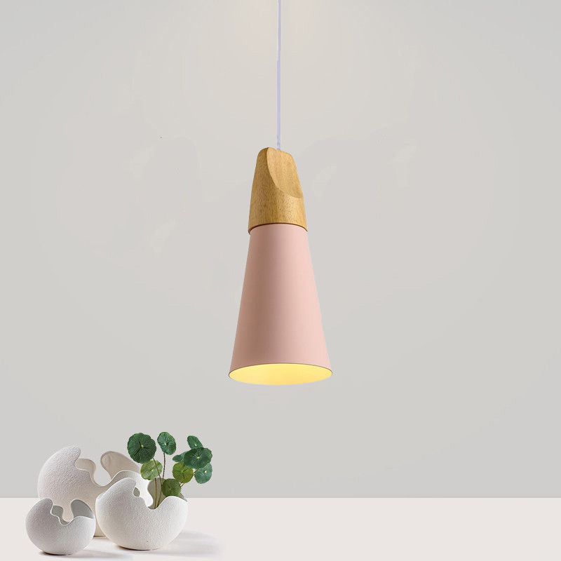 A slim pink Clérachic cone pendant with its wood top is lit and shown against a soft grey wall.