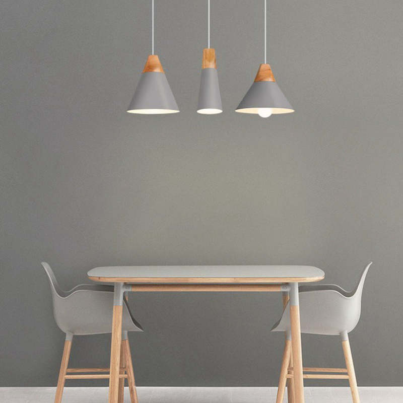 Three grey Clérachic cone pendants in mixed sizes hang together over a dining table against a grey wall.