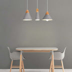 Three grey Clérachic cone pendants in mixed sizes hang together over a dining table against a grey wall.