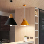 Black and yellow wide Clérachic cone pendants are lit side by side above a light wood kitchen counter.