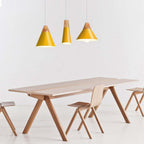 Three yellow Clérachic cone pendants in mixed sizes hang together above a pale oak dining table.