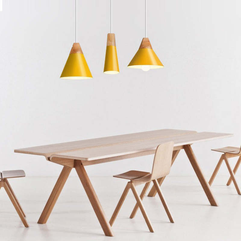 Three yellow Clérachic cone pendants in mixed sizes hang together above a pale oak dining table.