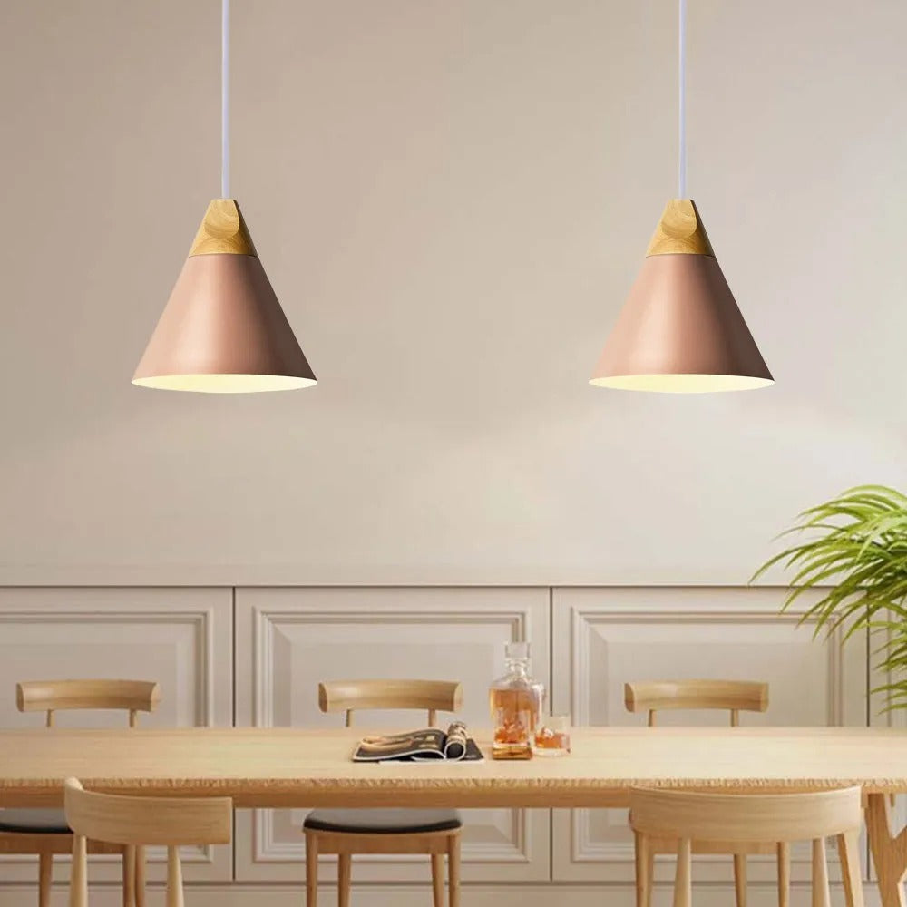 Two pink Clérachic cone pendants, wide shades and wood caps, hang above a light wood table in a cream dining room.