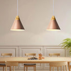 Two pink Clérachic cone pendants, wide shades and wood caps, hang above a light wood table in a cream dining room.