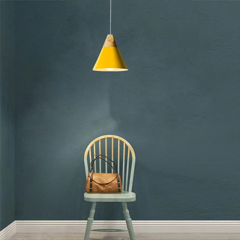 A yellow wide Clérachic cone pendant glows against a dark teal wall beside a chair holding a leather bag.