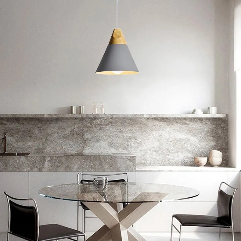 A grey wide Clérachic cone pendant hangs above a round glass dining table in a marble-backsplash kitchen.