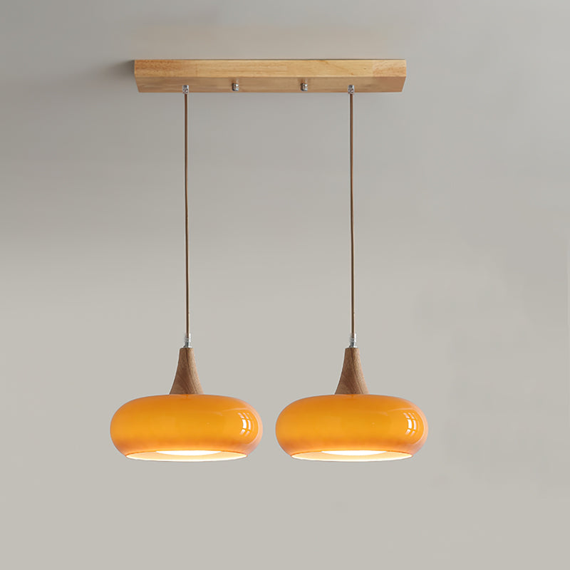 Two amber heads of the Clérachic Wood-Top Glass Pendant Light lit along a straight wood bar, spaced for a breakfast counter.