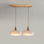 Two opal white heads of the Clérachic Wood-Top Glass Pendant Light on the wood bar, warm light pooling from each open rim.