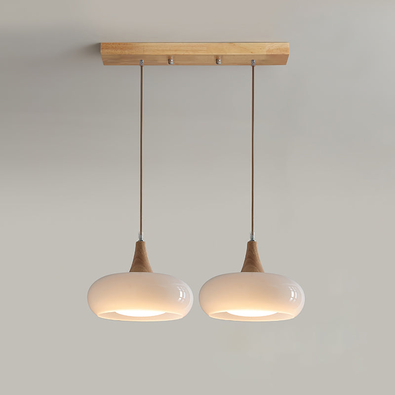 Two opal white heads of the Clérachic Wood-Top Glass Pendant Light on the wood bar, warm light pooling from each open rim.