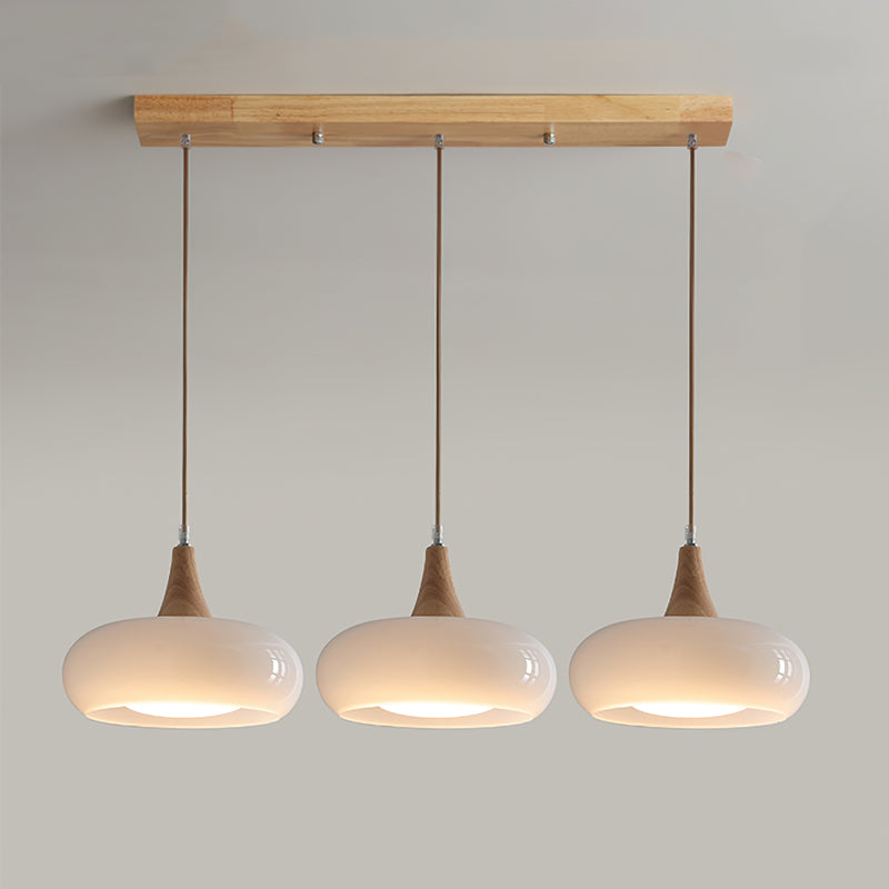 The three-head opal white Clérachic Wood-Top Glass Pendant Light, shades glowing in a row beneath the natural wood bar.