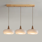 The three-head opal white Clérachic Wood-Top Glass Pendant Light, shades glowing in a row beneath the natural wood bar.