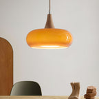 Amber Clérachic Wood-Top Glass Pendant Light hung low over a wooden dining table, its glossy shade catching the window light.