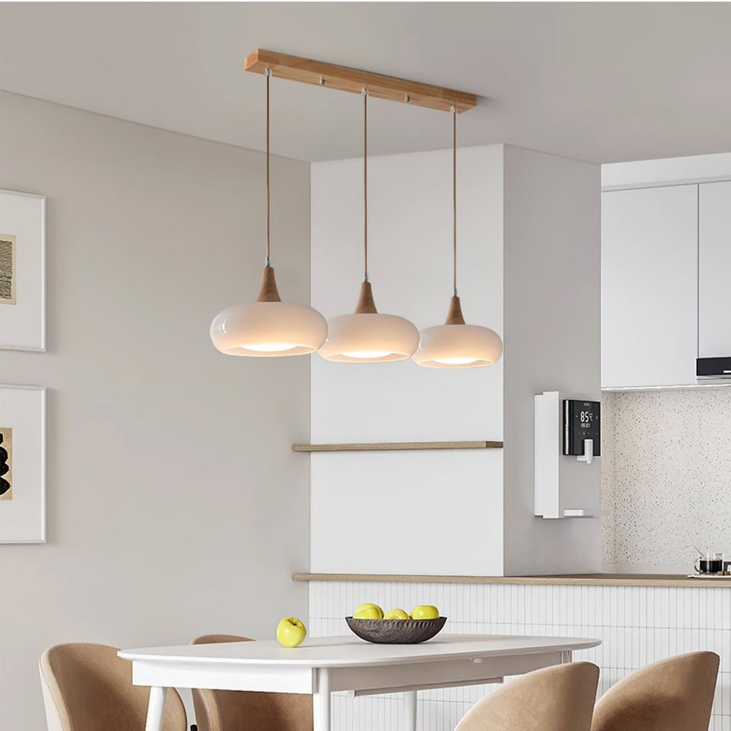 Three opal white Clérachic Wood-Top Glass Pendant Light heads lighting a white dining table in an open kitchen.