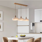 Three opal white Clérachic Wood-Top Glass Pendant Light heads lighting a white dining table in an open kitchen.