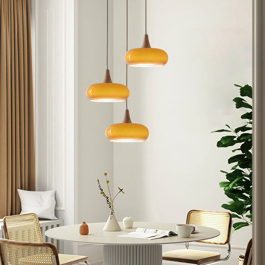 Three amber Clérachic Wood-Top Glass Pendant Light heads staggered at different drops over a round table with rattan chairs.