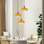 Three amber Clérachic Wood-Top Glass Pendant Light heads staggered at different drops over a round table with rattan chairs.