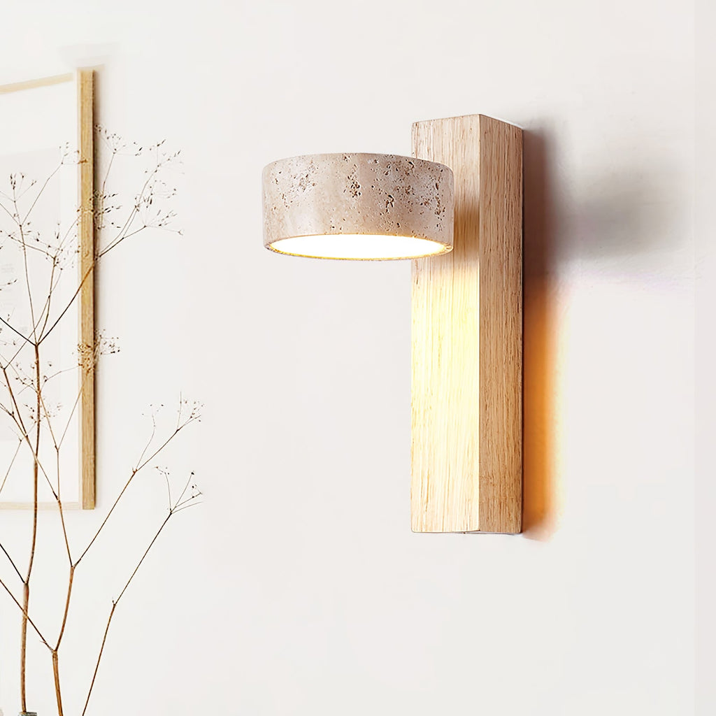 A Clérachic wall light in a pale wood finish, with a travertine head, lit softly in front of a white wall and dried twigs.