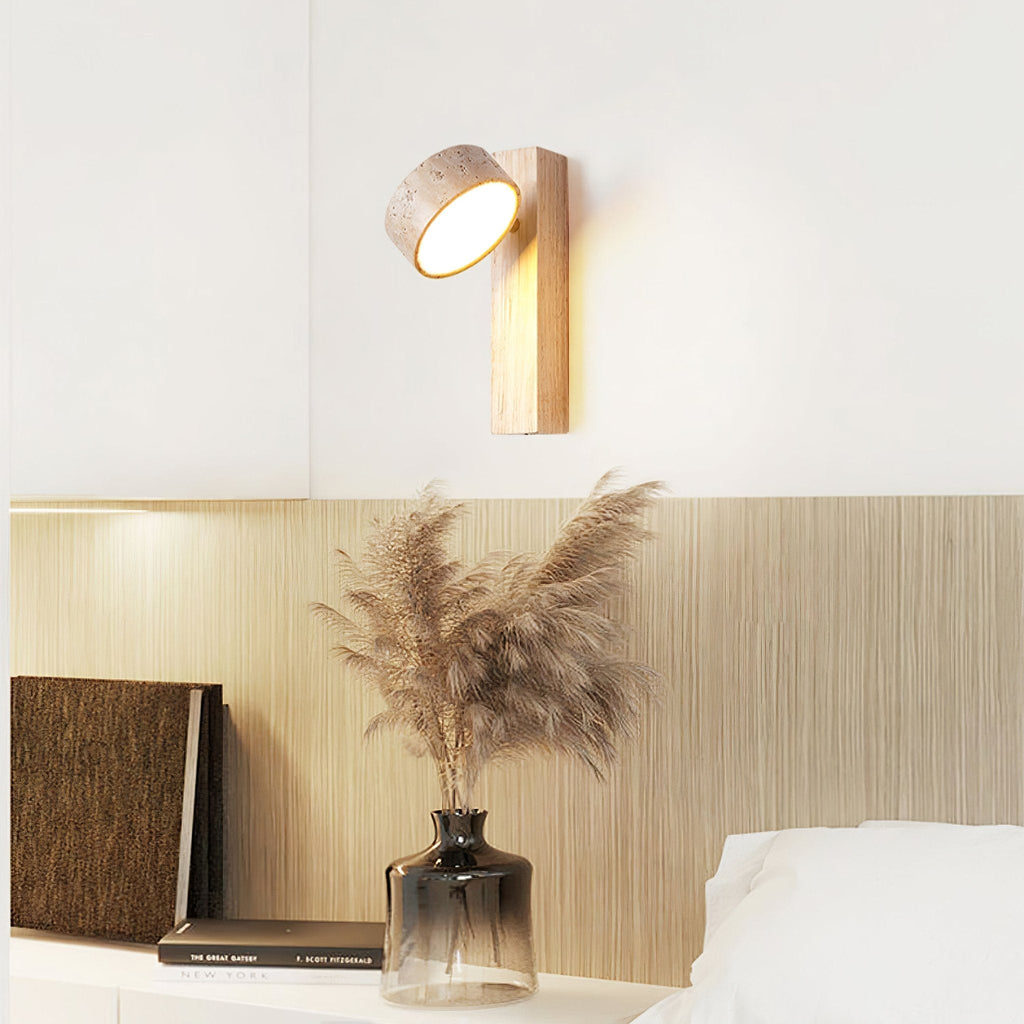Mounted above a bedside shelf with pampas grass in a glass vase, this Clérachic wall light has a pale wood bar and its travertine head tilted up.