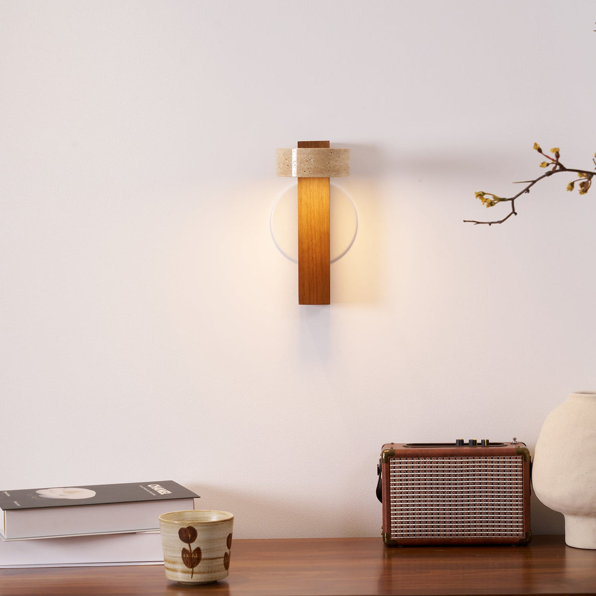 A small Clérachic wall light glows above a wooden console holding a retro radio, a cup, books and a cream vase.